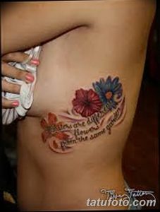 Фото татуировки на боку с изображением цветка и надписи "Flowers are different from the same garden". Цветной рисунок в нежной пастельной гамме.