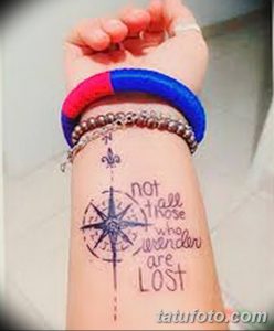 Фото татуировки на запястье с изображением компаса и цитаты "not all those who wander are LOST". Минималистичный стиль.