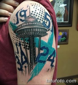 Фото тату на предплечье с изображением Space Needle в стиле акварель, с брызгами краски и цифрами. Оригинальный рисунок татуировки.