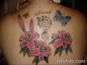 Фото тату: на спине изображены розовые лилии, отпечаток детской ноги и надпись 'Josiah'. Татуировка посвящена ребенку.