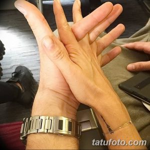 Фотография мужской руки с серебряными часами и небольшим тату на запястье. Рука слегка приподнята, демонстрируя татуировку.