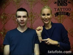 Фотография мужчины и женщины в тату-салоне. Женщина показывает свою татуировку 'Love' на запястье мастеру тату. Красный фон и логотип тату-салона.