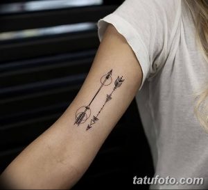 Черно-белая татуировка стрелы на предплечье, выполненная в минималистичном стиле с геометрическими элементами и кругом.