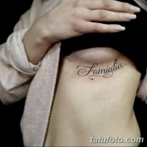 Фото тату надписи 'Famiglia' на боку женщины. Черный контур, каллиграфический шрифт, минималистичный дизайн. Идеально для любителей лаконичных татуировок.