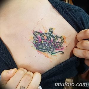 Фото маленькой татуировки на груди: акварельная корона в нежных розовых и фиолетовых тонах. Изящный и женственный дизайн.