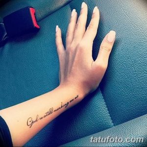Фото тату с надписью «God is still working on me» на руке. Черный цвет, каллиграфический шрифт, религиозный смысл, символ веры и надежды.