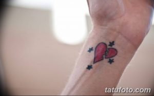 Фото тату на запястье, изображающее разбитое сердце, состоящее из двух половинок, с добавлением звезд. Черно-красная татуировка, эмоциональный дизайн.