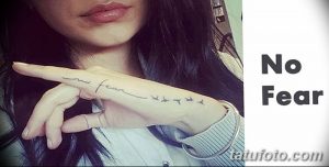 Фото тату: надпись "no fear" и силуэты летящих птиц на запястье девушки. Черный контур, минималистичный стиль.