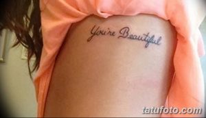 Фото тату на боку с надписью 'You're Beautiful', выполненной каллиграфическим шрифтом черными чернилами.
