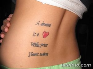 Фото тату надписи 'A dream Is a Wish your Heart makes' с изображением красного сердца на женском боку. Черно-белый рисунок татуировки с ярким акцентом.