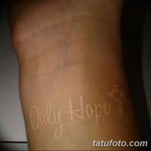 Фото тату надписи 'Only Hope' с маленьким крестом на руке, выполненной черными чернилами. Символичный рисунок татуировки, выражающий веру и надежду.
