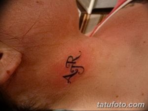 Фото тату на шее: изящные инициалы 'R' и 'A', выполненные в каллиграфическом стиле. Небольшой и элегантный рисунок.