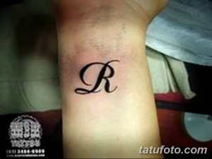 Фото тату: черная татуировка буквы 'R' на запястье. Классический дизайн, выполненный четкими линиями.