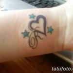 Фото тату: небольшое тату на запястье, изображающее сердце с буквой 'R' внутри, окруженное голубыми звёздами. Цветная татуировка в мультяшном стиле.