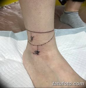 Фото тату: минималистичный браслет из точек с буквами 'y' и 'M' на женской лодыжке. Черно-белая татуировка, выполненная тонкими линиями.