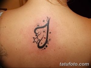 Фото тату: маленькая татуировка буквы 'J', украшенной звездами и точками, на спине девушки. Минималистичный и женственный дизайн.