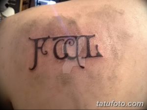 Фото татуировки на спине: инициалы 'FCGL', выполненные в готическом стиле, черные чернила, теневые эффекты.