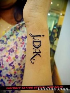 Фото татуировки на запястье: надпись 'IDK' (I Don't Know) в стильном шрифте, черные чернила, дерзкий дизайн.