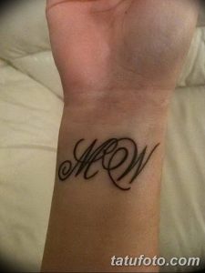 Фото татуировки на запястье: изящные инициалы 'MW', выполненные в черном цвете, каллиграфический стиль, женственный дизайн.