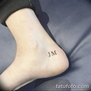 Фото тату с инициалами 'JM' на лодыжке, выполненное тонкими черными линиями.