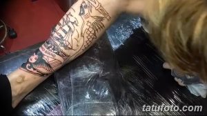 Фото тату: мастер наносит татуировку на руку клиента. Виден эскиз с изображением корабля, морских волн и других морских элементов.