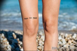 Фото тату с надписью "ENJOY THE MOMENT" на колене. Минималистичный шрифт и лаконичный дизайн.
