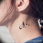 Фото татуировки на шее, изображающей стилизованную букву 'A' с маленьким сердечком, выполненной в черном цвете.