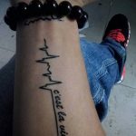 Фото татуировки на запястье, изображающей кардиограмму и фразу 'c'est la vie', выполненной в черном цвете.