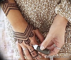 Фото процесса нанесения татуировки хной на руку, мастер наносит узор с помощью конуса, видны детали рисунка.