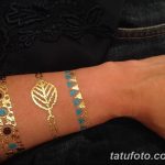 Фото тату в виде золотых браслетов на запястье, с изображением листа и геометрических фигур, на фоне темной ткани.