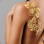 Фото тату: крупные золотые пионы, расположенные на спине, создают эффект роскошного украшения и подчеркивают красоту женской фигуры.