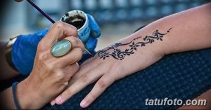 Фото тату мехенди: мастер наносит узоры хной на руку девушки, демонстрируя процесс создания временной татуировки.