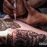 Фото тату: мастер наносит рисунок мехенди на ногу клиента. Детализированный узор, традиционные инструменты и процесс создания красивой татуировки.