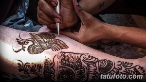 Фото тату: мастер наносит рисунок мехенди на ногу клиента. Детализированный узор, традиционные инструменты и процесс создания красивой татуировки.