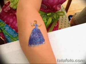 Фото тату с изображением девочки в пышном синем платье, украшенном блестками. Татуировка нанесена на внутреннюю сторону предплечья.