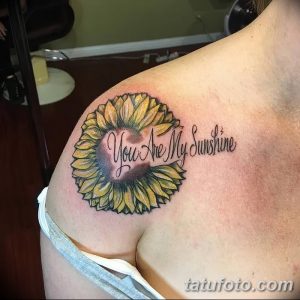 Фото тату с изображением яркого подсолнуха и надписью 'You Are My Sunshine' на плече. Цветная татуировка в реалистичном стиле.