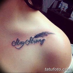 Фото тату: на ключице девушки изображена вдохновляющая надпись "Stay Strong" с изображением пера. Рисунок татуировки выполнен в черном цвете.