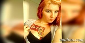 Фото тату: яркая и необычная татуировка с логотипом Skittles и разноцветными конфетами на женской груди. Оригинальный рисунок татуировки.