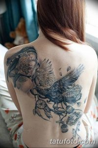 Фото тату ворона, летящего над портретом девушки с ловцом снов, на спине. Черно-серый рисунок с детальной проработкой перьев и лица.