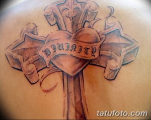 Фото татуировки на плече с изображением креста, сердца и надписи "Divinity". Детализированный рисунок татуировки выполнен в черно-серых тонах.