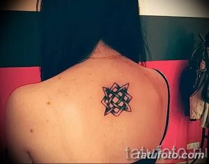 Фото небольшой татуировки кельтского узла на спине девушки. Рисунок выполнен в черном цвете, с четкими контурами и геометрическим орнаментом.