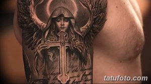 Фото тату на руке: реалистичное изображение ангела с распростертыми крыльями, держащего крест. Черно-серый рисунок с высокой детализацией.