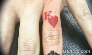 Фото тату: маленькая красная татуировка с изображением карты 'Король' и сердца на пальце руки. Символ любви и преданности.