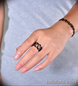 Фото женской татуировки, имитирующей кружевной браслет на пальце и переходящий в кружевной узор на запястье. Черный рисунок на светлой коже.