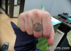 Фотография татуировки на пальце руки с изображением символа группы Pink Floyd. Черно-белый рисунок, минималистичный дизайн, музыкальная тематика.