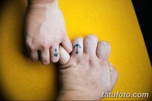 Фотография парных татуировок с изображением якоря и стрелы на пальцах, выполненных в синем цвете.