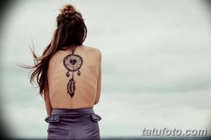 Фото тату: Черно-белый рисунок ловца снов с одним пером на спине девушки. Минималистичный и элегантный дизайн.