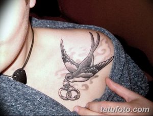 Фото тату ласточки, держащей в клюве кандалы. Рисунок выполнен в черно-серых тонах с детальной проработкой перьев и металла.