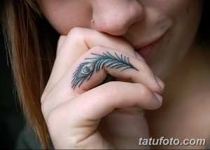 Фото тату: маленькое, изящное изображение пера павлина в черно-серых тонах на пальце руки.