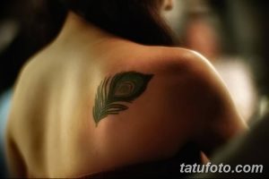 Фото тату: небольшое перо павлина на плече, выполненное в ярких зеленых и синих тонах. Минималистичный и стильный рисунок татуировки.